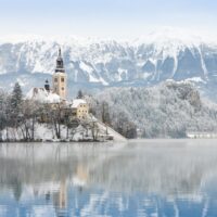 church and snow covered mountains reflected Lake Bled Slovenia